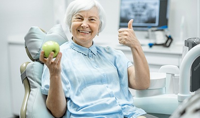 a dental implant patient smiling and holding an apple