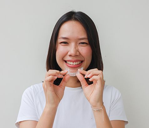 a patient smiling and holding her Invisalign aligner